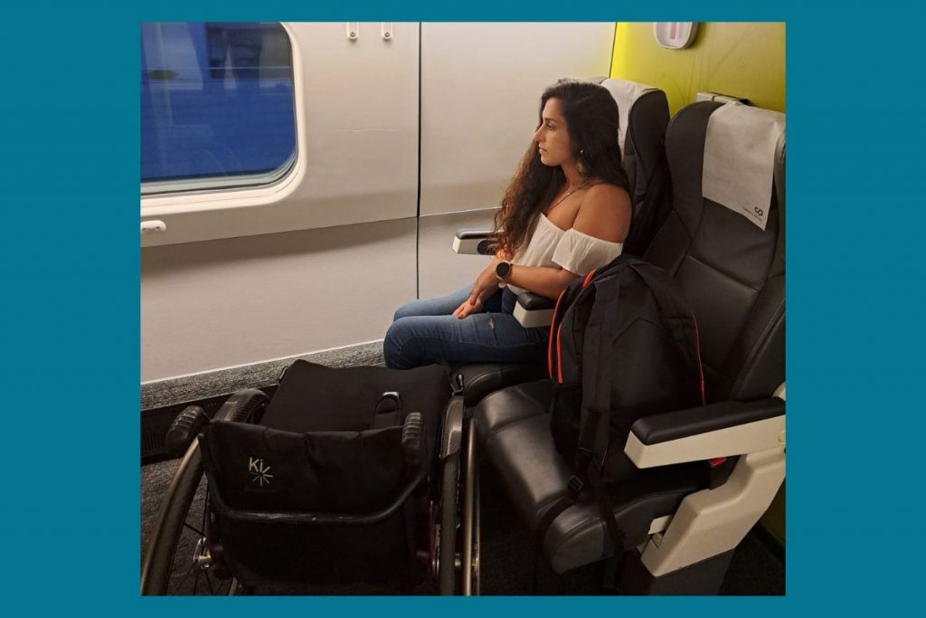 Oessoa sentada num comboio. Existe uma cadeira de rodas perto da pessoa.