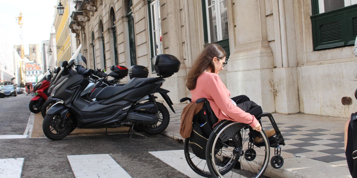 Mulher de cadeira de rodas a tentar subir um passeio na cidade
