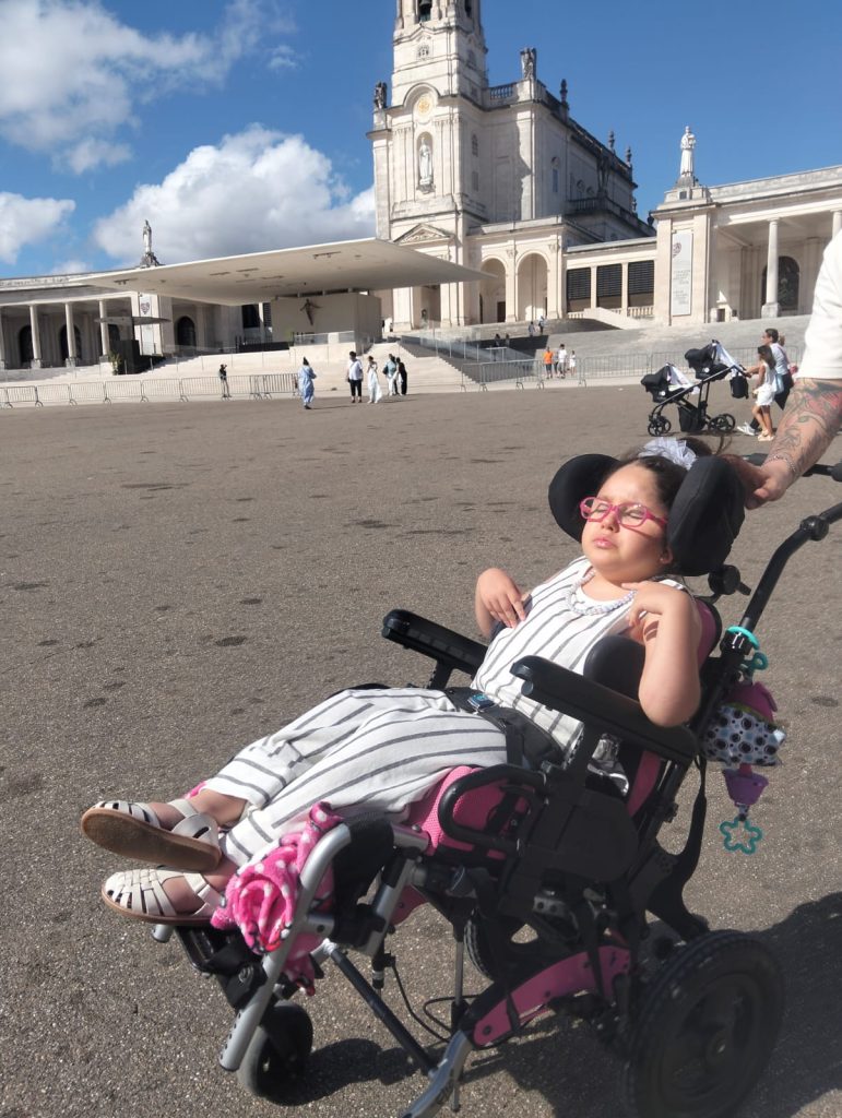 Menina em cadeira de rodas em frente ao santuário de Fátima